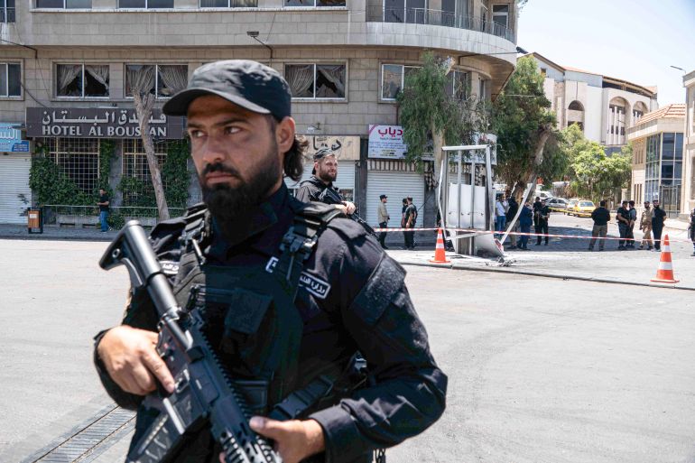 An armed man stands in front of a building.