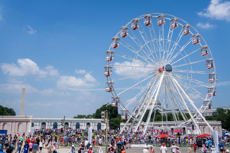 As military aircraft fly past, attendees walk at the Great American State Fair on the National Mall, Friday, July 3, 2026, in Washington. (AP Photo/Allison Robbert)