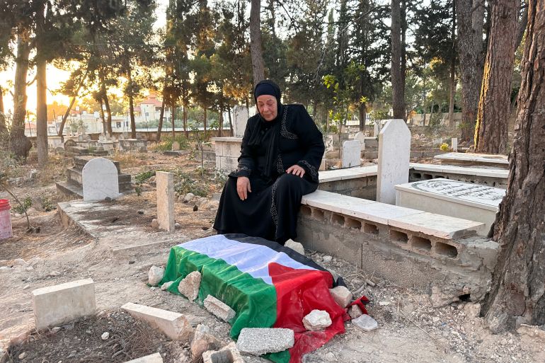 A woman sits beside a grave draped in a Palestinian flag.